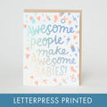 A square greeting card with a kraft envelope behind it, featuring the phrase “Awesome people make Awesome BABIES!” in pastel blue, green, and peach lettering with small baby-themed icons. A blue banner at the bottom reads “LETTERPRESS PRINTED.