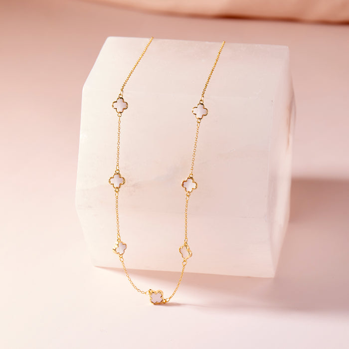 Gold necklace with clover-shaped pendants on a pink background