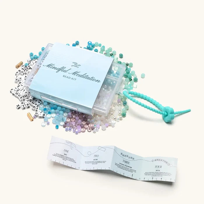 "Mindful Meditation" bead kit with scattered colourful beads, letter beads, teal cord, and an unfolded instruction booklet.
