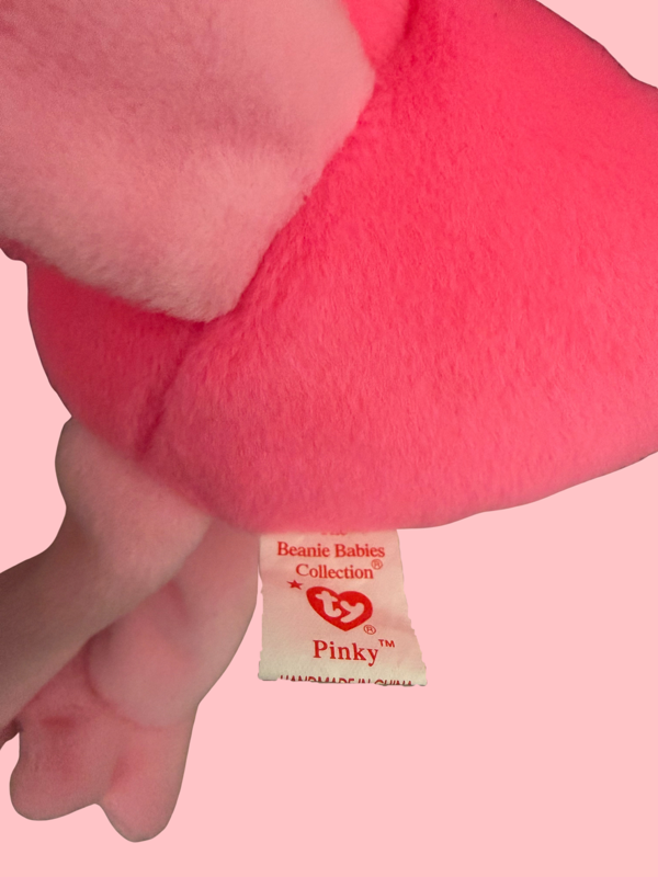 Close-up of a pink plush toy with a label on a pink background