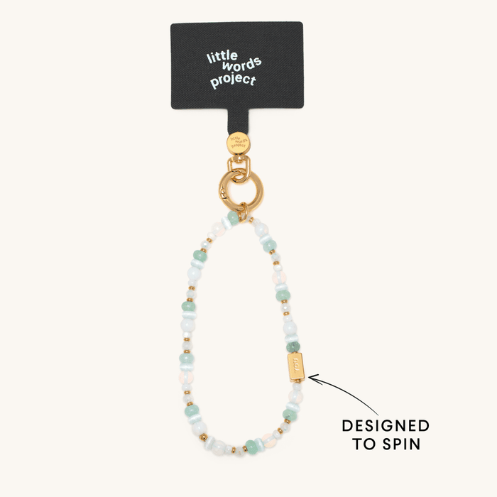 Little Words Project beaded phone strap in soft blue, white, and gold tones with a spinning gold bar charm.