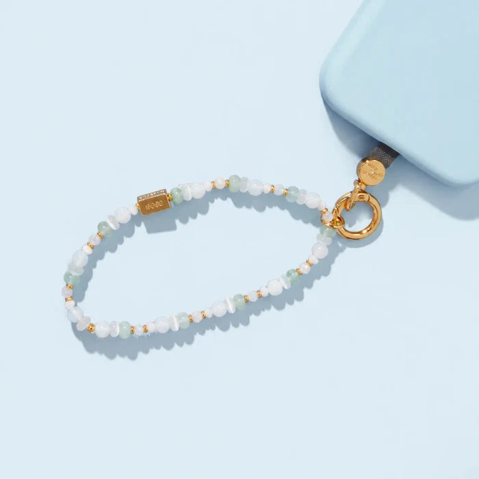 Beaded phone strap in soft white and mint tones with a gold bar charm and ring clasp, attached to a light blue phone case.